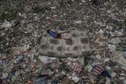 Ένα παιδί που συλλέγει σκουπίδια, ξαπλωμένο σε στρώμα σε δρόμο των Φιλιππίνων, που έχει τόσα απόβλημα όπου ακόμα και το περπάτημα σε αυτόν είναι δύσκολο.